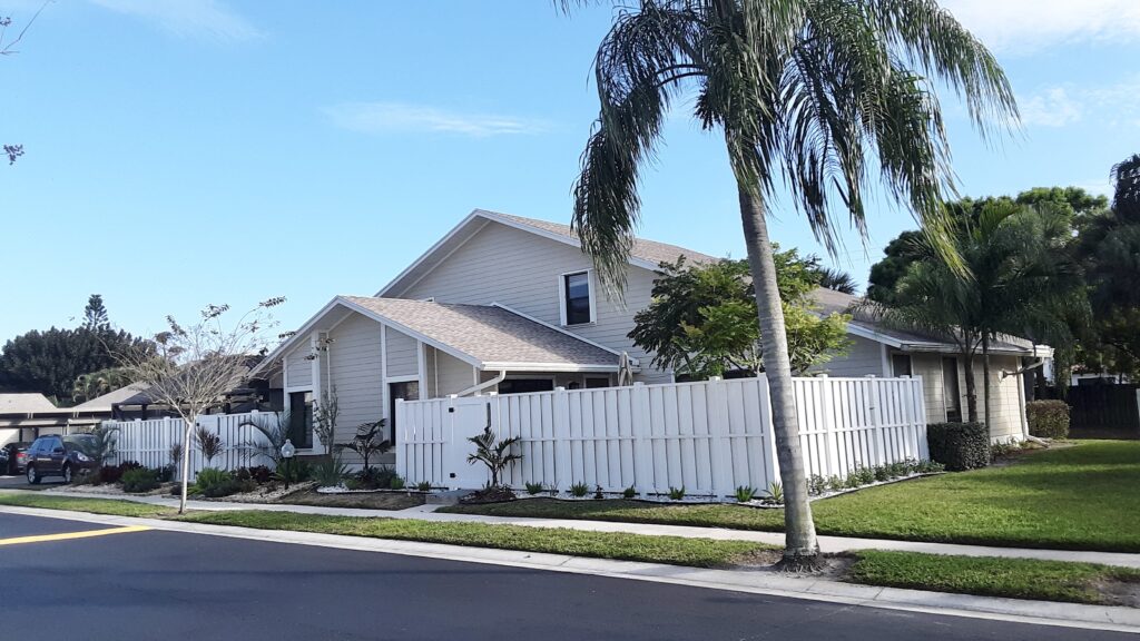 A house with gray tiled roof with tall white fence and gate